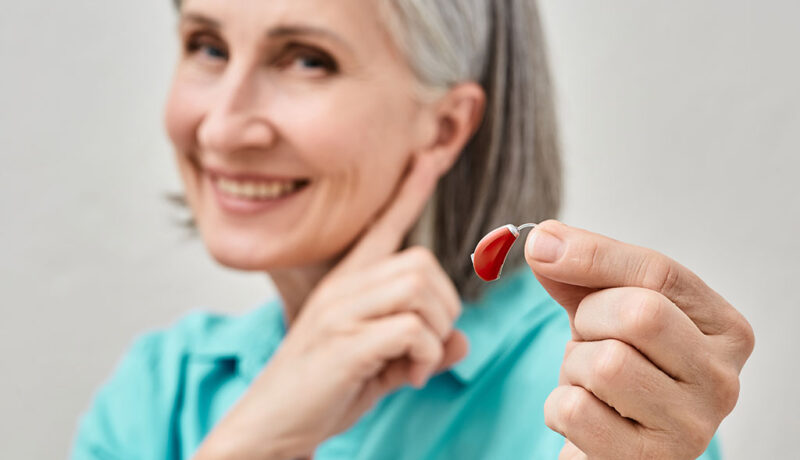 An Elderly Woman Experiencing Age-Related Hearing Loss Holding A Hearing Aid In Her Hand