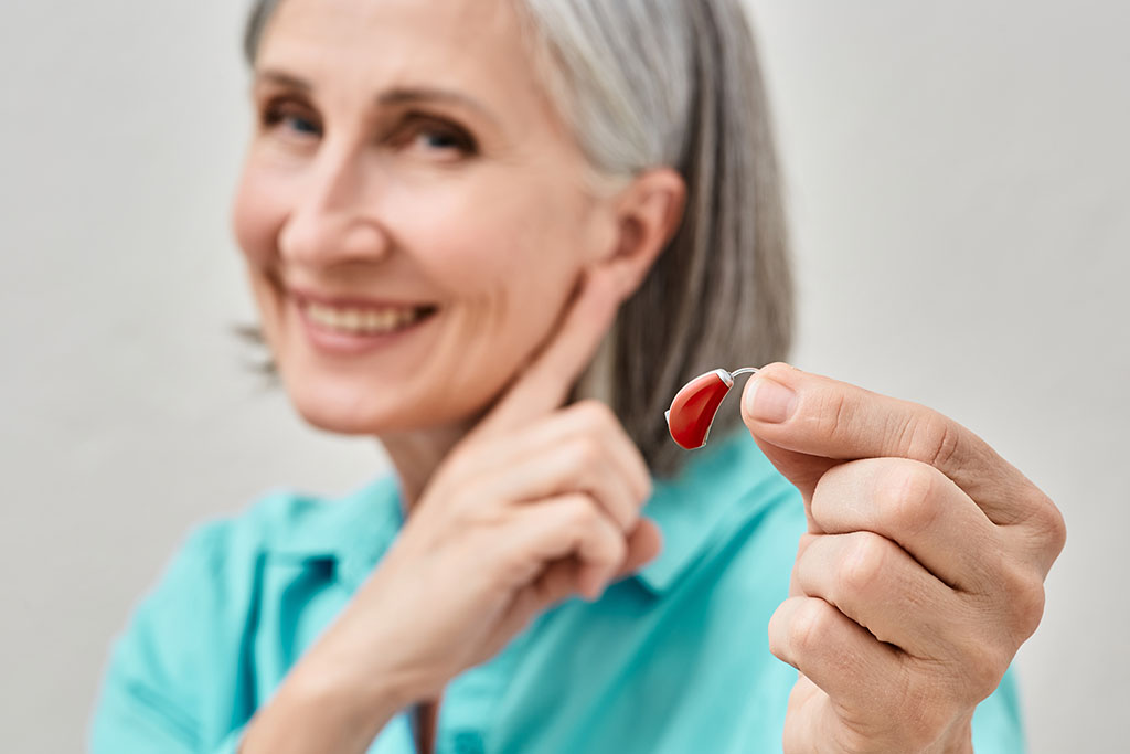 An Elderly Woman Experiencing Age-Related Hearing Loss Holding A Hearing Aid In Her Hand