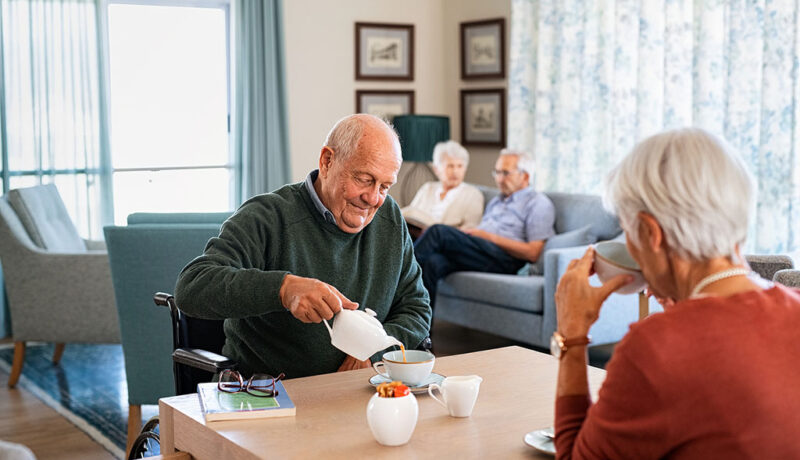 A Senior Man Sitting at a Table Pouring From a Teapot With a Senior Woman Across From Him What Does a Memory Care Community Do