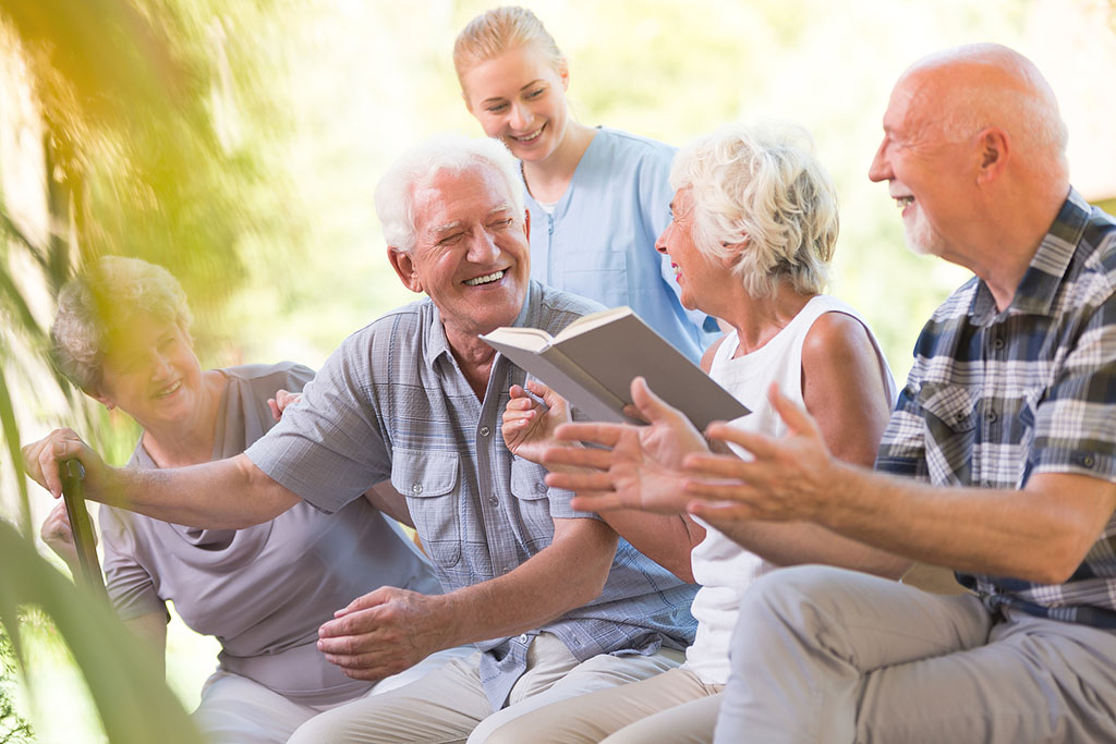 A Group Of Senior Adults Laughing While Looking Through A Book Together Social Isolation In Seniors